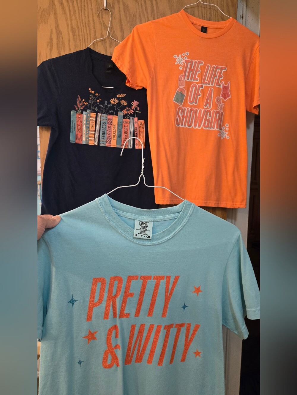 3 Taylor Swift T Shirts. 1 Is Navy, 1 Is Orange And 1 Is Mint Green.